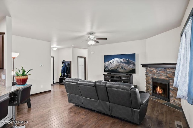 living area with visible vents, dark wood finished floors, a stone fireplace, and ceiling fan