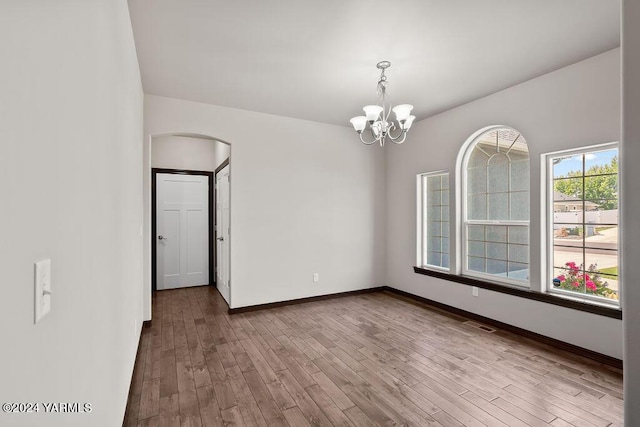 empty room featuring a chandelier, arched walkways, wood finished floors, visible vents, and baseboards