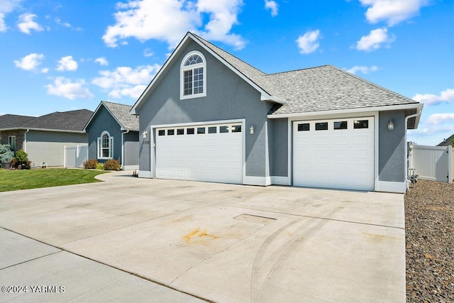 traditional home with a garage, a shingled roof, fence, concrete driveway, and stucco siding