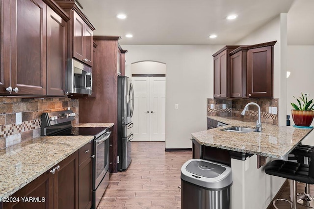 kitchen featuring arched walkways, light stone counters, stainless steel appliances, a sink, and a kitchen breakfast bar