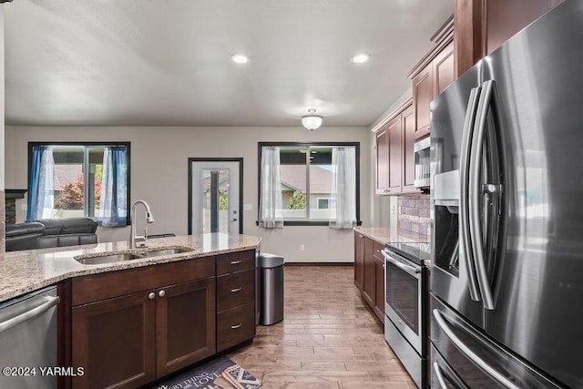 kitchen featuring tasteful backsplash, light wood-style flooring, light stone countertops, stainless steel appliances, and a sink