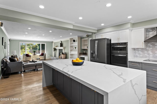 kitchen featuring multiple ovens, light stone counters, open floor plan, and stainless steel fridge with ice dispenser