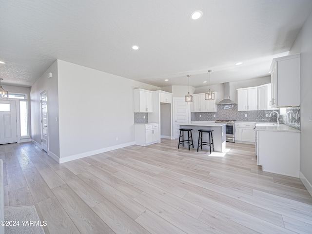 kitchen with a kitchen island, white cabinetry, light countertops, wall chimney exhaust hood, and stainless steel range