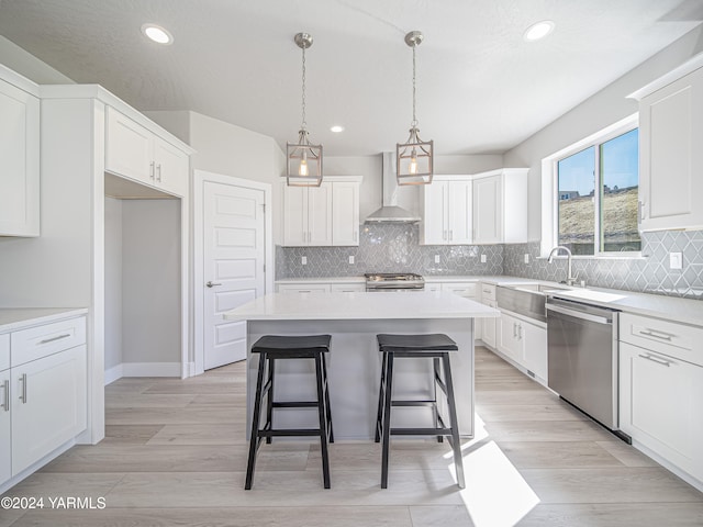 kitchen with stainless steel appliances, light countertops, wall chimney exhaust hood, and white cabinetry
