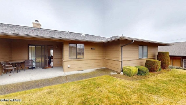 back of house featuring a yard, a shingled roof, a chimney, and a patio area