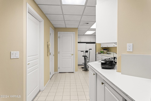 kitchen featuring light tile patterned floors, a paneled ceiling, light countertops, white cabinetry, and white fridge