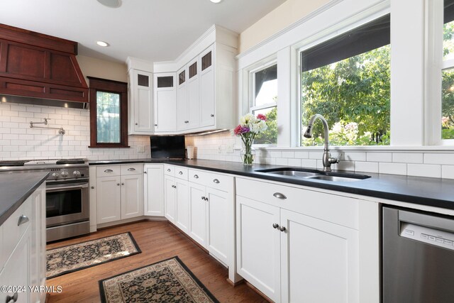 kitchen with stainless steel appliances, a sink, white cabinets, dark countertops, and glass insert cabinets