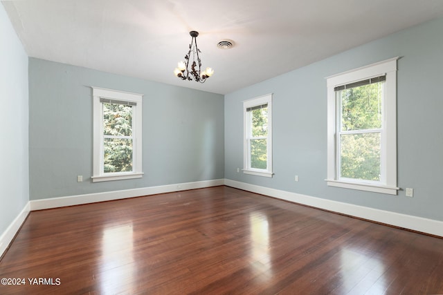 spare room with dark wood-style floors, a healthy amount of sunlight, visible vents, and an inviting chandelier