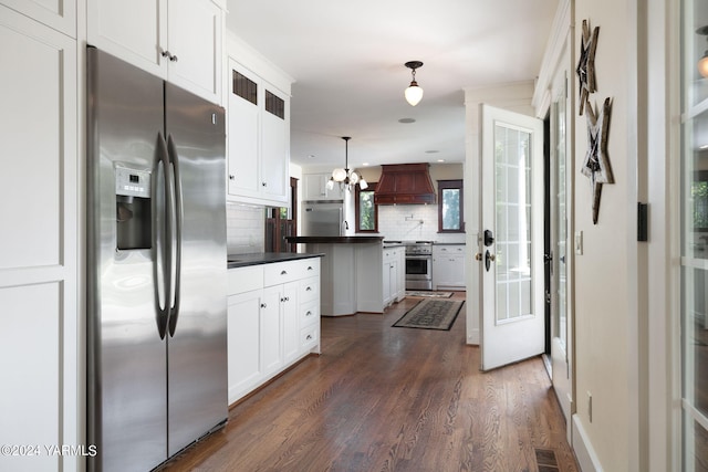 kitchen featuring white cabinets, dark countertops, appliances with stainless steel finishes, decorative light fixtures, and custom exhaust hood