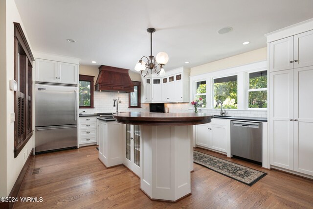 kitchen featuring white cabinetry, appliances with stainless steel finishes, dark countertops, glass insert cabinets, and custom range hood