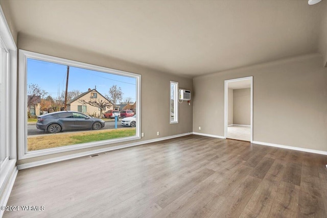 spare room with visible vents, a wall mounted AC, light wood-style flooring, and baseboards