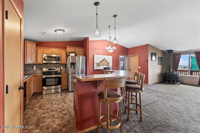 3501 S 40th Ave, Yakima, WA 98903 - kitchen featuring appliances with stainless steel finishes, a wood stove, a breakfast bar, vaulted ceiling, and tasteful backsplash