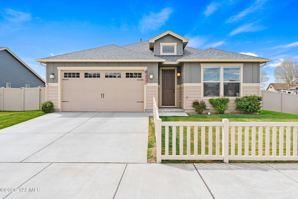 prairie-style home featuring fence, a shingled roof, a front lawn, concrete driveway, and a garage