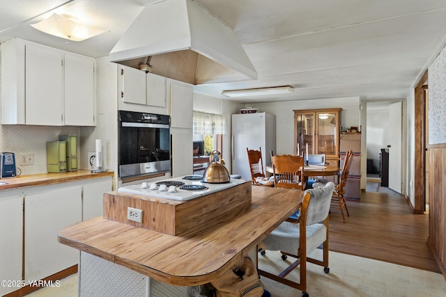 kitchen featuring custom exhaust hood, decorative backsplash, white cabinetry, butcher block countertops, and white appliances