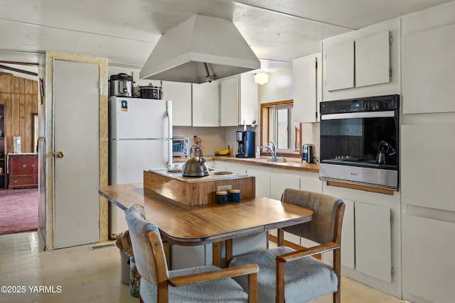 kitchen with freestanding refrigerator, white cabinets, stovetop, and island range hood