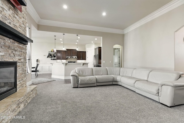 living area featuring arched walkways, ornamental molding, a stone fireplace, recessed lighting, and wood finished floors