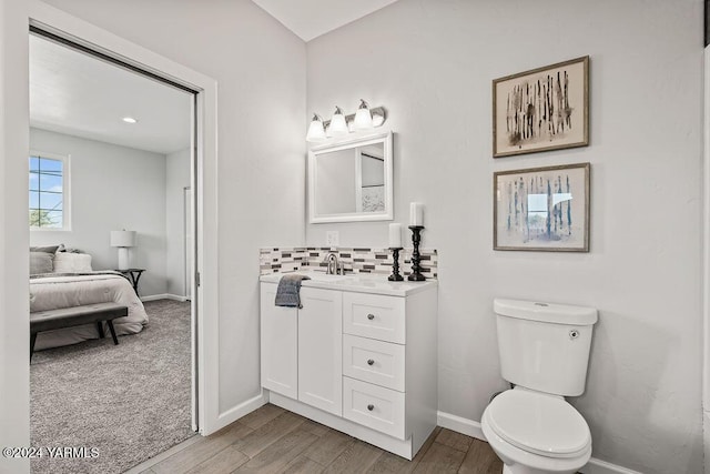 bathroom with connected bathroom, toilet, wood finished floors, vanity, and backsplash