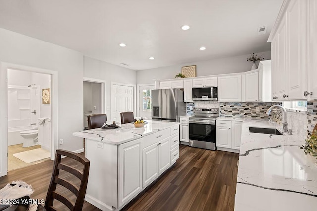 kitchen with light stone counters, a kitchen island, a sink, white cabinets, and appliances with stainless steel finishes