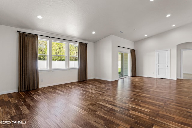 spare room featuring healthy amount of natural light, dark wood-style floors, arched walkways, lofted ceiling, and recessed lighting