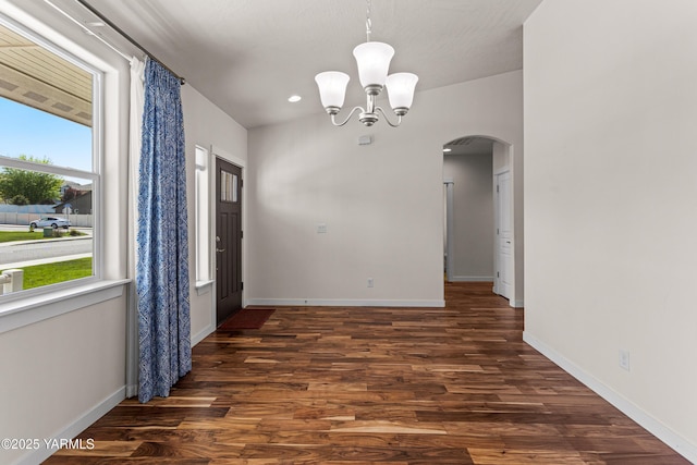 unfurnished dining area with arched walkways, dark wood-type flooring, and baseboards