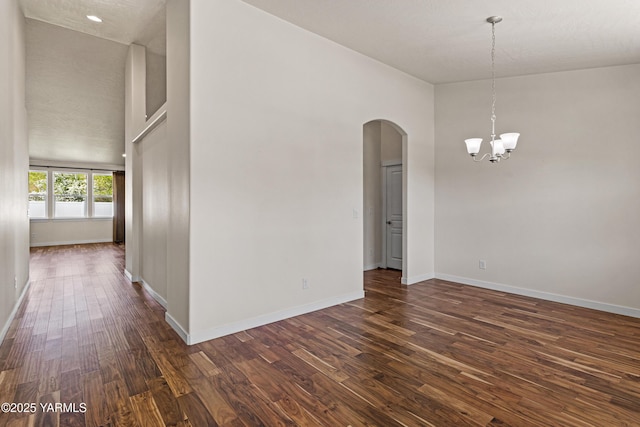 empty room with arched walkways, dark wood-style floors, a chandelier, baseboards, and a high ceiling
