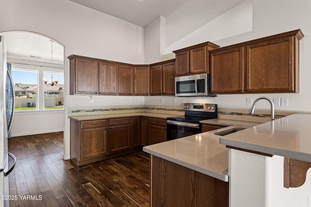kitchen featuring stainless steel appliances, a peninsula, dark wood finished floors, a sink, and a chandelier