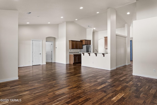 unfurnished living room featuring high vaulted ceiling, dark wood-type flooring, arched walkways, baseboards, and recessed lighting