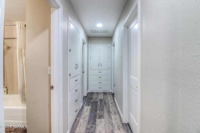 corridor with visible vents, wood finished floors, and a textured wall