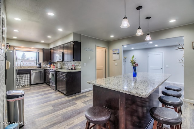 kitchen featuring stainless steel appliances, light wood-style floors, backsplash, and a kitchen breakfast bar