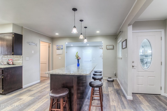 kitchen featuring backsplash, a kitchen island, a kitchen breakfast bar, light wood-type flooring, and baseboards