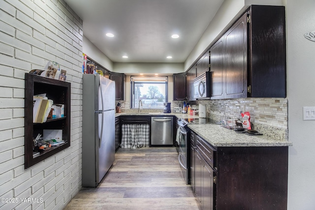 kitchen featuring stainless steel appliances, a sink, light wood-type flooring, decorative backsplash, and light stone countertops