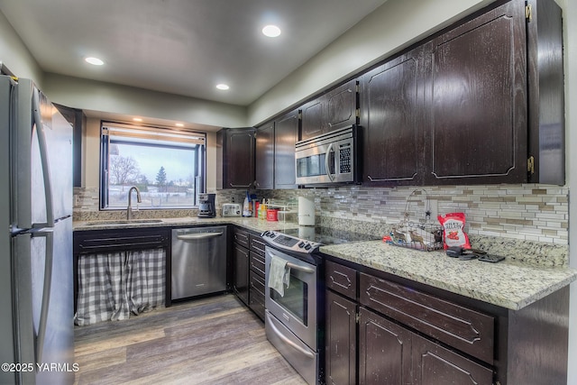 kitchen featuring light wood finished floors, appliances with stainless steel finishes, a sink, and tasteful backsplash