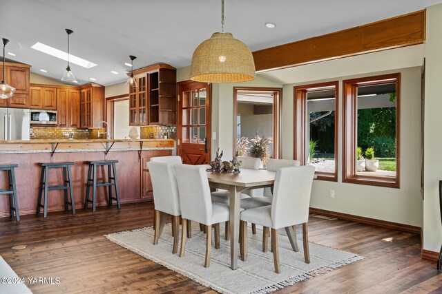 dining space featuring lofted ceiling with skylight, recessed lighting, dark wood finished floors, and baseboards