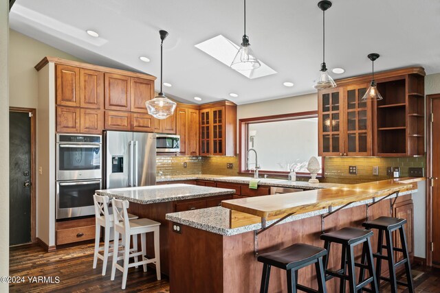 kitchen with light stone counters, appliances with stainless steel finishes, a breakfast bar, and glass insert cabinets