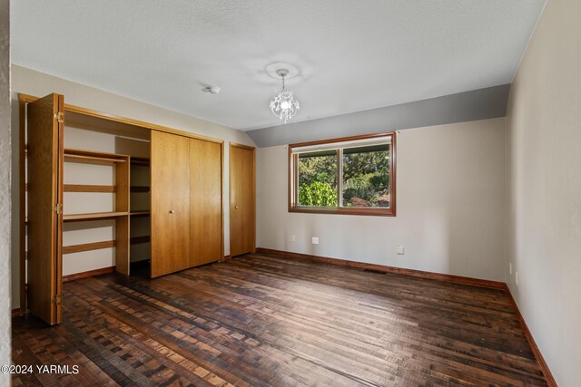 unfurnished bedroom with dark wood-style floors, a chandelier, vaulted ceiling, and baseboards