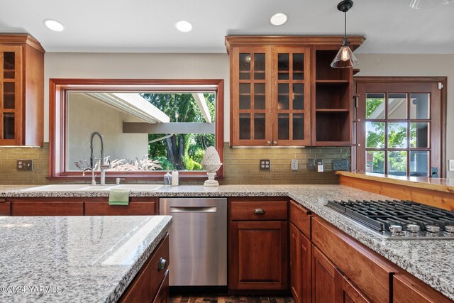 kitchen featuring appliances with stainless steel finishes, a sink, glass insert cabinets, and light stone countertops