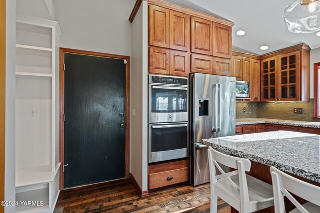 kitchen featuring tasteful backsplash, dark wood-style floors, glass insert cabinets, light stone countertops, and stainless steel appliances