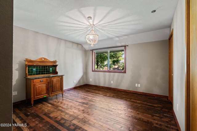 empty room with lofted ceiling, baseboards, dark wood finished floors, and a notable chandelier