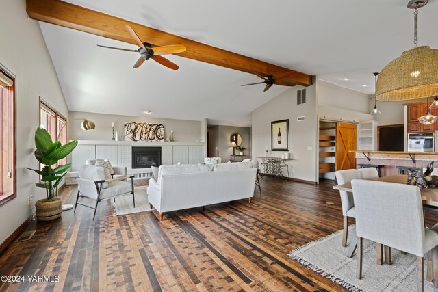 living area with a barn door, visible vents, a glass covered fireplace, dark wood-style flooring, and beamed ceiling