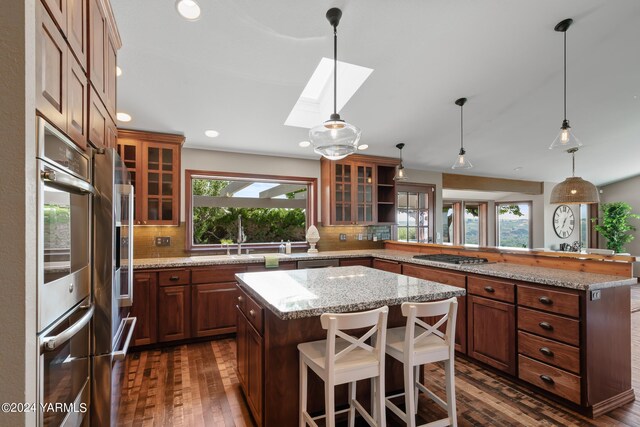 kitchen with a peninsula, a kitchen island, glass insert cabinets, and stainless steel appliances