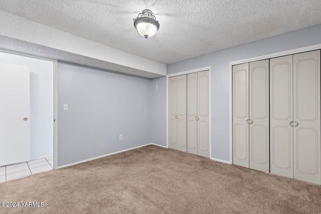 unfurnished bedroom featuring light tile patterned floors, a textured ceiling, two closets, and light colored carpet