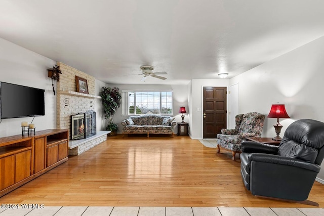 living room featuring a brick fireplace, light wood-style flooring, and a ceiling fan