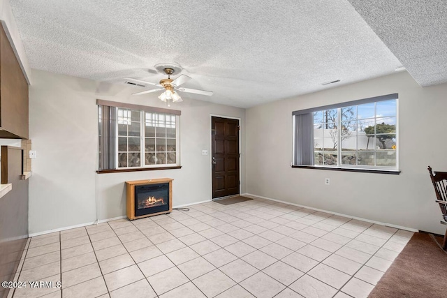 unfurnished living room featuring a glass covered fireplace, visible vents, ceiling fan, and light tile patterned floors