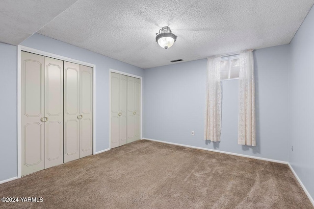 unfurnished bedroom featuring a textured ceiling, visible vents, multiple closets, and carpet flooring