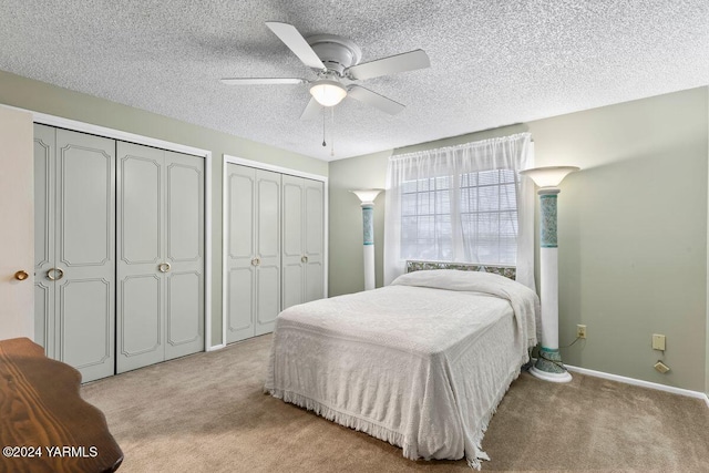 bedroom featuring light carpet, a textured ceiling, two closets, and baseboards