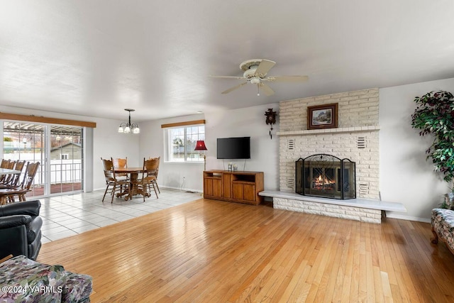 living area featuring ceiling fan with notable chandelier, a brick fireplace, light wood-style flooring, and baseboards