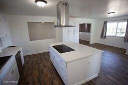 kitchen with black electric stovetop, dark wood-type flooring, a kitchen island, white cabinets, and island exhaust hood