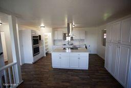 kitchen featuring dark wood-type flooring, extractor fan, stainless steel double oven, light countertops, and white cabinetry