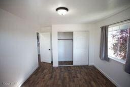 unfurnished bedroom with a closet, dark wood finished floors, and baseboards