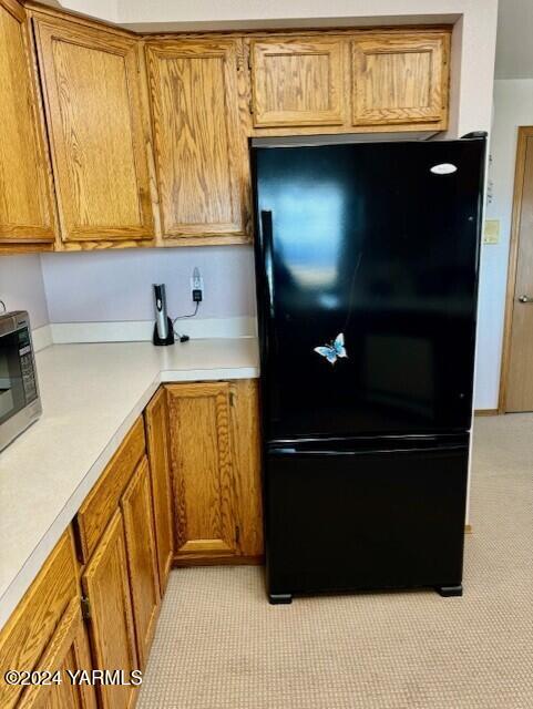 kitchen featuring brown cabinets, stainless steel microwave, light countertops, and freestanding refrigerator